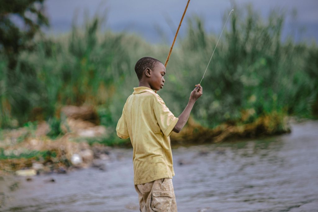 pexels-photo-11031552-11031552 A young boy skillfully fishing with a stick by a lush riverbank, serene and focused.
